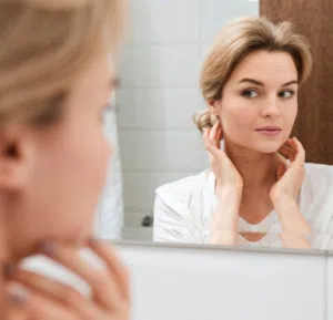 woman looking at skin in the mirror